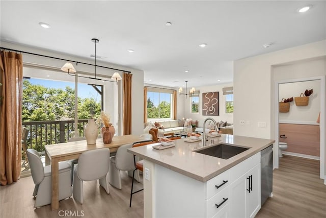 kitchen with a center island with sink, light wood-style flooring, white cabinets, a sink, and dishwasher