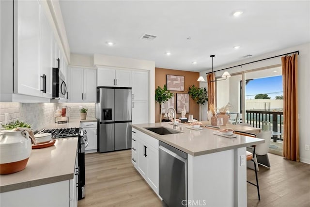 kitchen with stainless steel appliances, a sink, light wood finished floors, decorative backsplash, and white cabinets