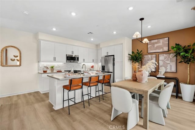 kitchen featuring stainless steel appliances, light wood-style flooring, tasteful backsplash, a kitchen bar, and recessed lighting