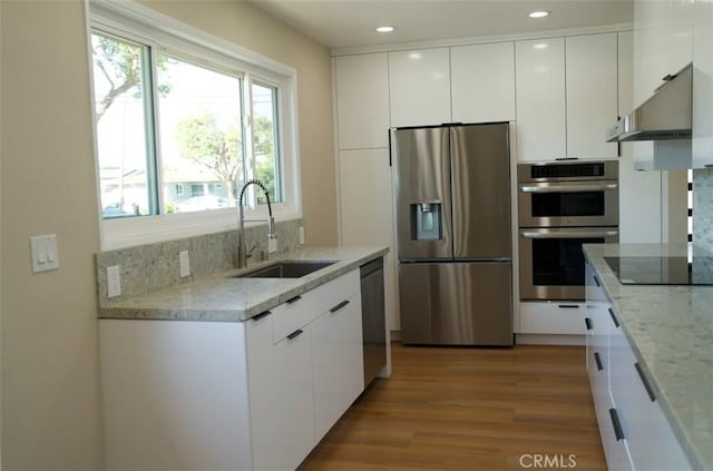 kitchen with light wood-style floors, appliances with stainless steel finishes, under cabinet range hood, white cabinetry, and a sink