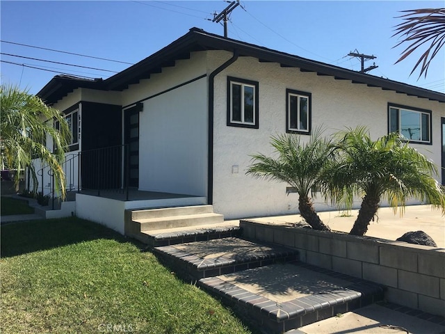 view of property exterior with entry steps, a lawn, and stucco siding