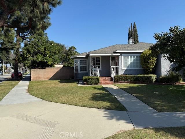 bungalow-style home with stucco siding, fence, and a front yard