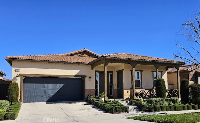 mediterranean / spanish home featuring a porch, a tile roof, concrete driveway, stucco siding, and an attached garage