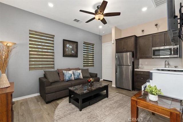 living room with ceiling fan, baseboards, visible vents, and light wood-style flooring