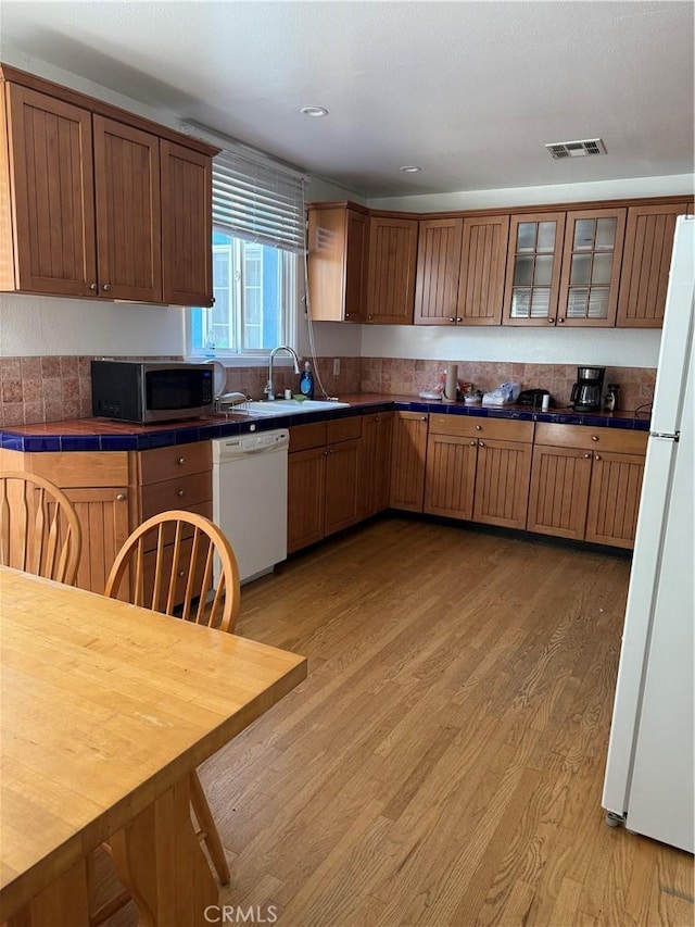 kitchen with white appliances, visible vents, glass insert cabinets, light wood-style floors, and a sink