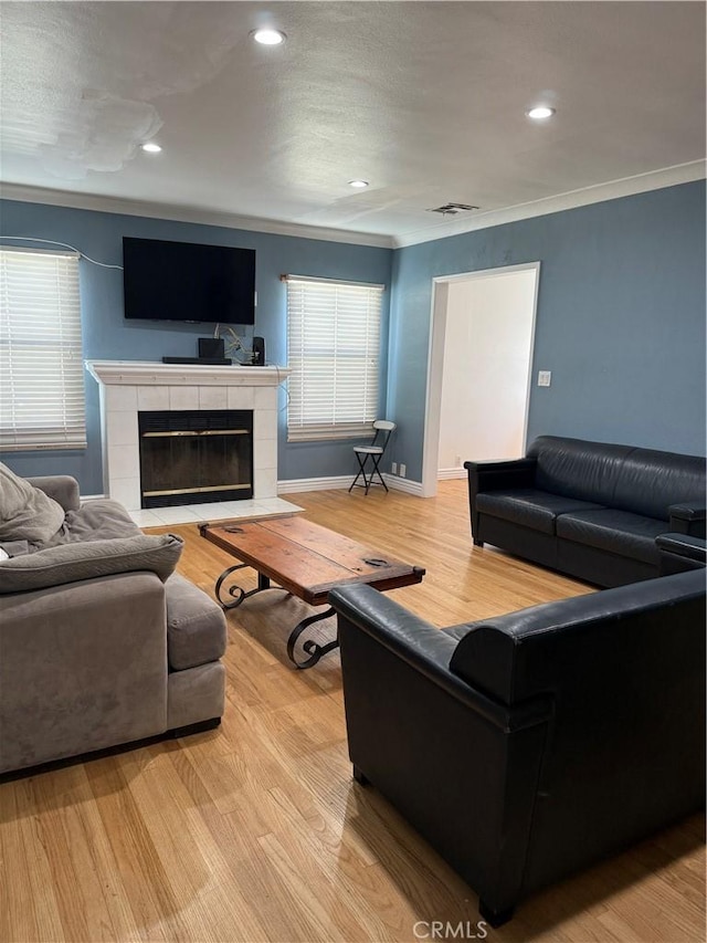 living room with visible vents, baseboards, light wood-style flooring, ornamental molding, and a fireplace