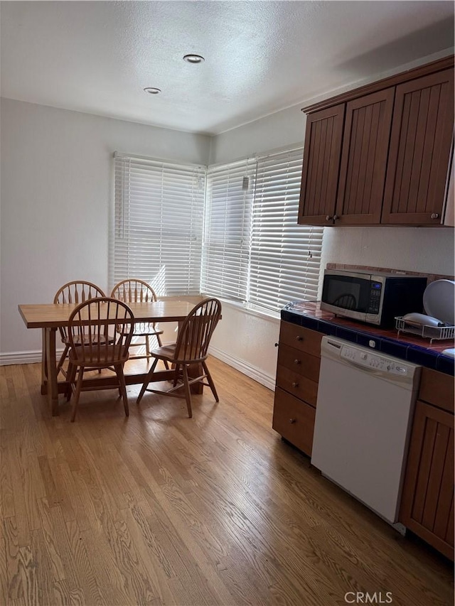 kitchen with tile countertops, light wood finished floors, white dishwasher, and stainless steel microwave