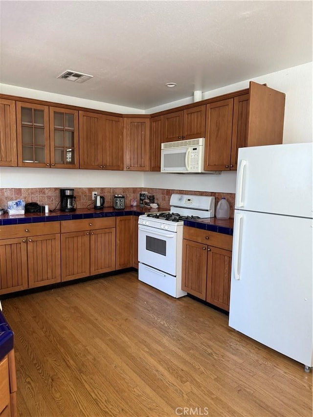 kitchen featuring tile counters, white appliances, brown cabinetry, and light wood-style floors