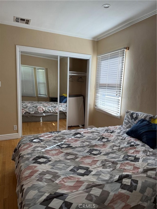 bedroom with ornamental molding, a closet, wood-type flooring, and visible vents