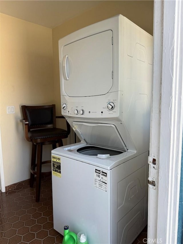 clothes washing area with laundry area, dark tile patterned flooring, and stacked washer / dryer