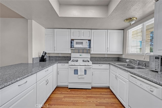 kitchen with light wood finished floors, white appliances, white cabinets, and a sink