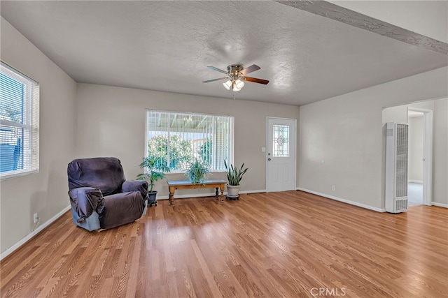 living area featuring light wood-type flooring, ceiling fan, a textured ceiling, and baseboards