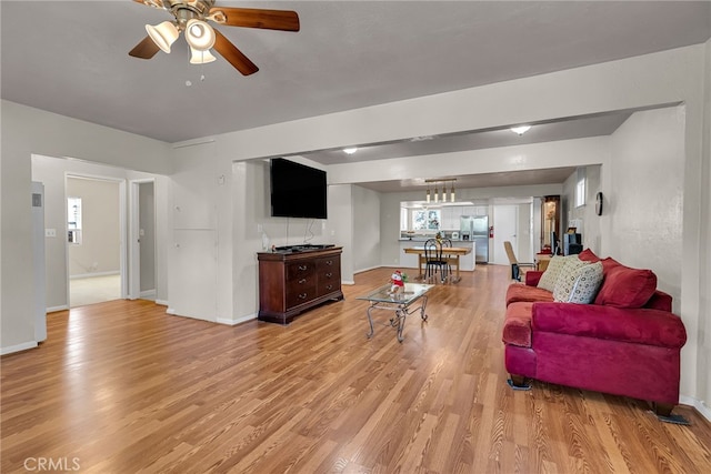 living room with baseboards, ceiling fan, and light wood-type flooring