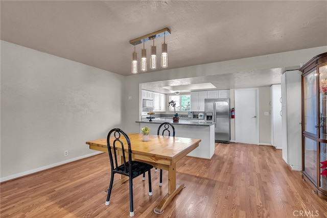 dining area with a textured ceiling, light wood-style flooring, and baseboards