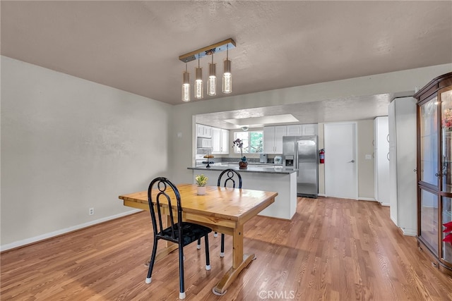 dining area with baseboards, light wood-style floors, and a textured ceiling