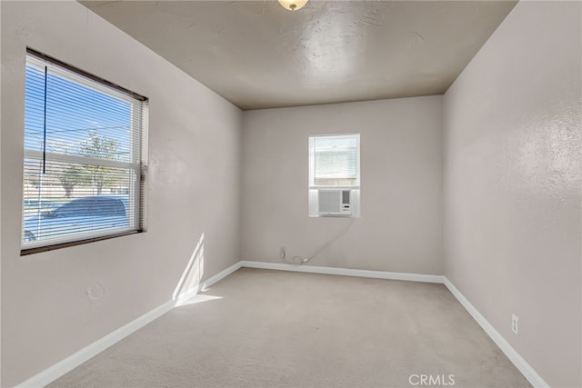 spare room featuring cooling unit, light colored carpet, and baseboards