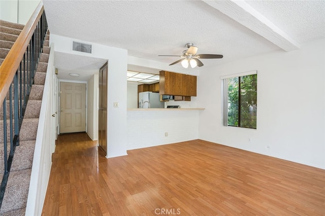 unfurnished living room featuring a textured ceiling, wood finished floors, visible vents, a ceiling fan, and stairs