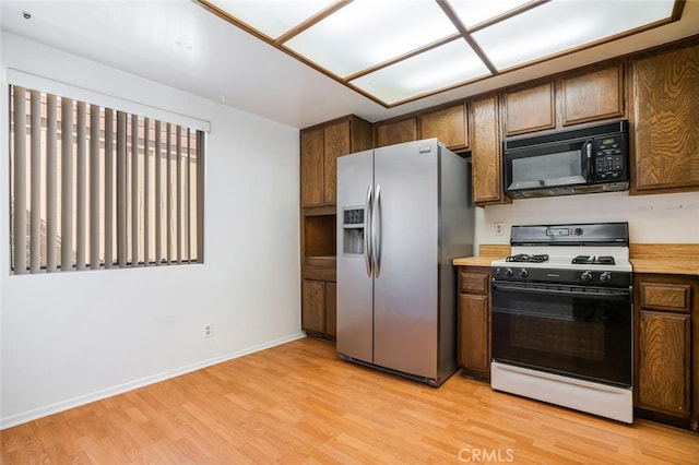 kitchen featuring range with gas stovetop, light wood finished floors, light countertops, black microwave, and stainless steel fridge