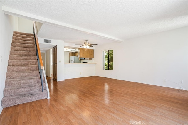 unfurnished living room featuring visible vents, wood finished floors, stairs, a textured ceiling, and beam ceiling