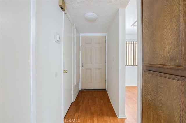 corridor with a textured ceiling, light wood-type flooring, and baseboards