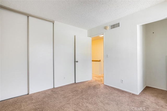 unfurnished bedroom with a textured ceiling, a closet, carpet flooring, and visible vents