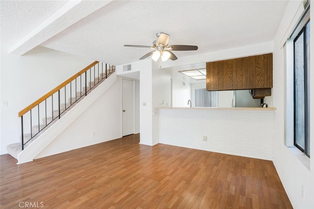 unfurnished living room featuring stairs, a textured ceiling, wood finished floors, and visible vents