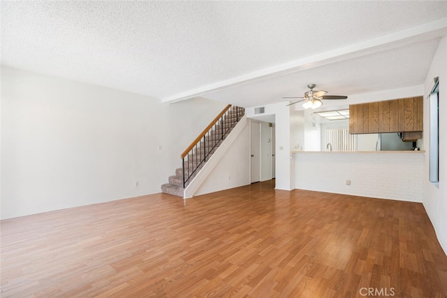 unfurnished living room featuring stairs, beamed ceiling, a textured ceiling, and wood finished floors