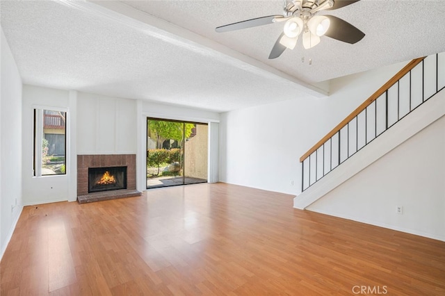 unfurnished living room with a brick fireplace, a textured ceiling, and wood finished floors