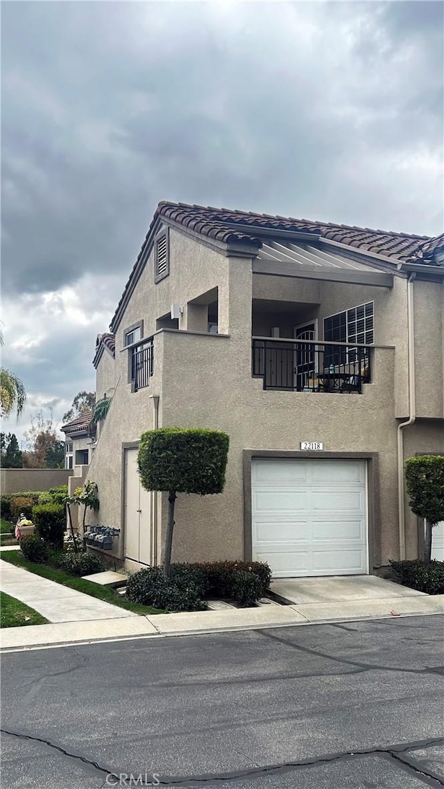 townhome / multi-family property with a tile roof, a balcony, and stucco siding