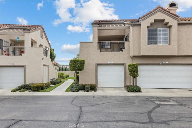 view of property featuring an attached garage, a tile roof, and stucco siding