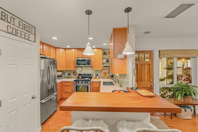 kitchen with stainless steel appliances, visible vents, light wood-style flooring, a sink, and a peninsula