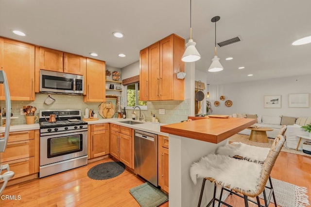 kitchen with light wood finished floors, visible vents, a kitchen bar, appliances with stainless steel finishes, and a sink