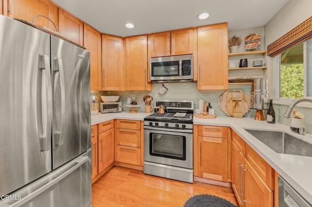 kitchen with light wood finished floors, a sink, decorative backsplash, light countertops, and stainless steel appliances