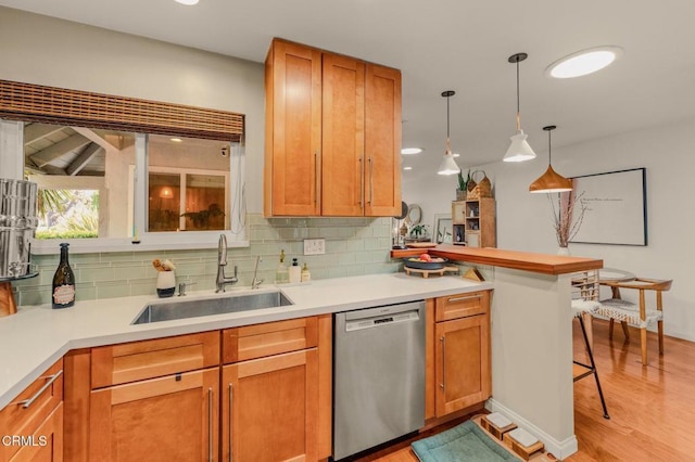 kitchen featuring a peninsula, light wood-style flooring, a sink, decorative backsplash, and stainless steel dishwasher