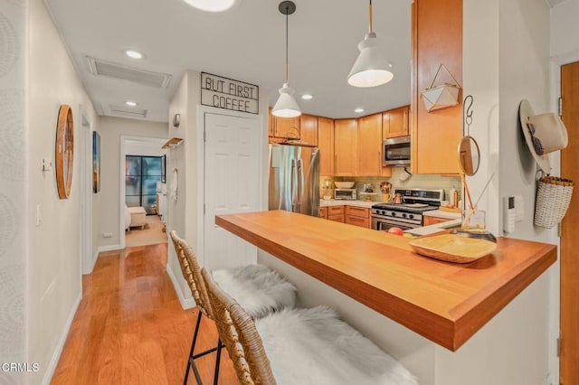 kitchen featuring light wood finished floors, backsplash, decorative light fixtures, a kitchen bar, and stainless steel appliances