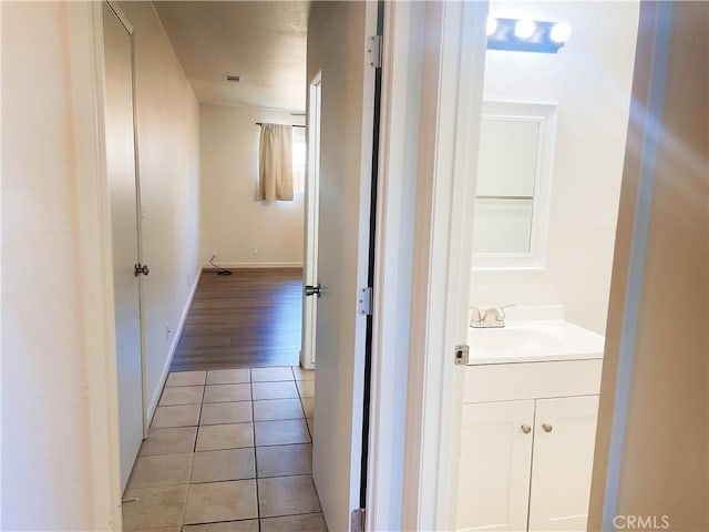 hall featuring light tile patterned floors, visible vents, baseboards, and a sink