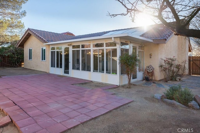 back of house with stucco siding, a sunroom, and a tiled roof