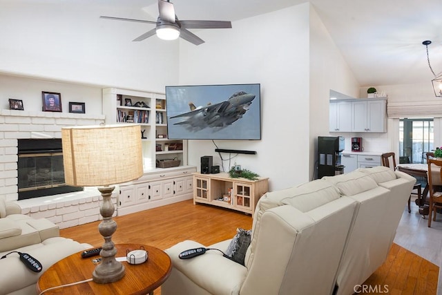 living area with light wood finished floors, ceiling fan, a fireplace, and vaulted ceiling