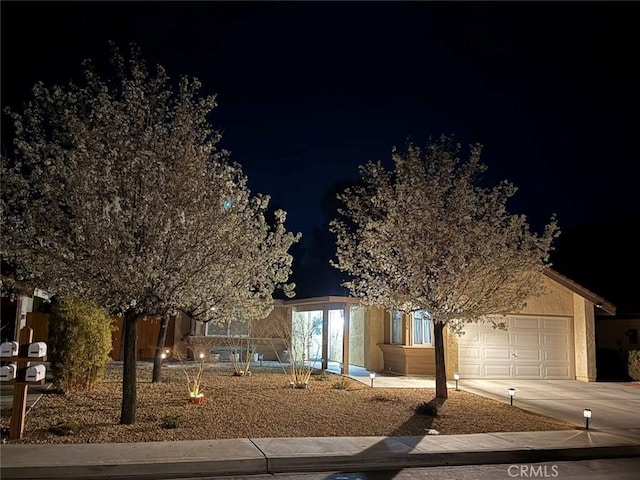 view of property hidden behind natural elements featuring concrete driveway, an attached garage, and stucco siding