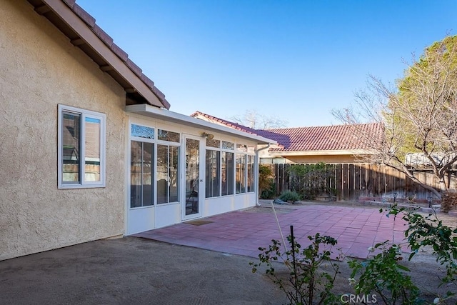 exterior space featuring a patio, fence, a sunroom, a tiled roof, and stucco siding