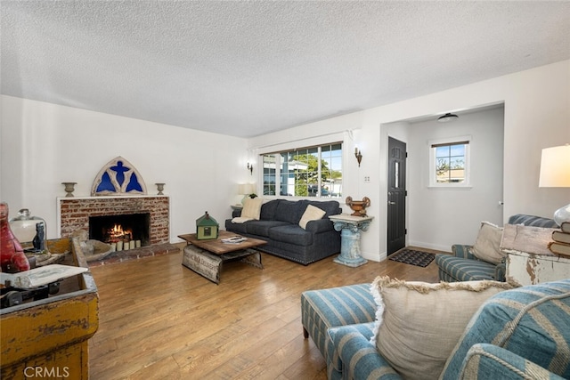 living area featuring a brick fireplace, a textured ceiling, baseboards, and wood finished floors