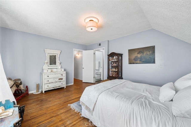 bedroom with visible vents, vaulted ceiling, a textured ceiling, wood finished floors, and baseboards