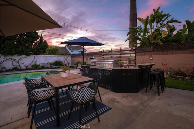 patio terrace at dusk with area for grilling, a fenced backyard, grilling area, outdoor dry bar, and outdoor dining area