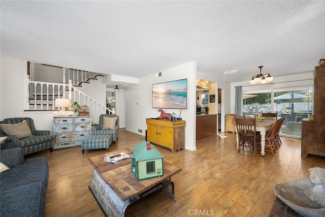 living room featuring a textured ceiling, stairway, hardwood / wood-style flooring, and a notable chandelier