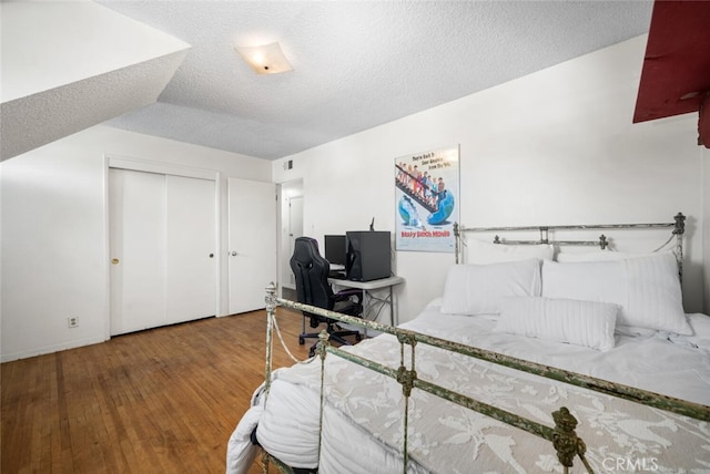 bedroom with a closet, a textured ceiling, visible vents, and wood finished floors