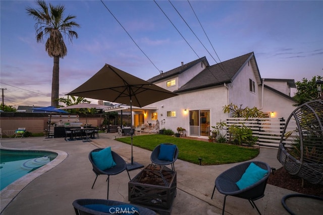 back of property at dusk with fence, a lawn, a fenced in pool, stucco siding, and a patio area