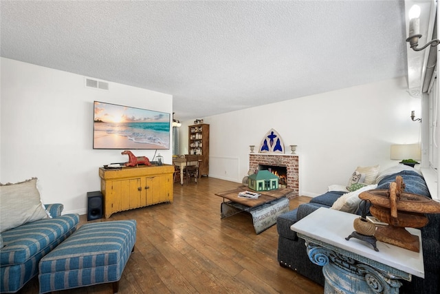 living room featuring baseboards, visible vents, hardwood / wood-style flooring, a textured ceiling, and a fireplace