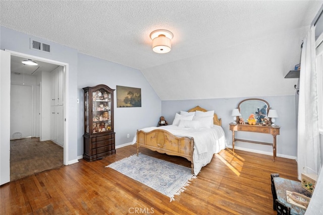 bedroom with attic access, visible vents, lofted ceiling, wood finished floors, and a textured ceiling