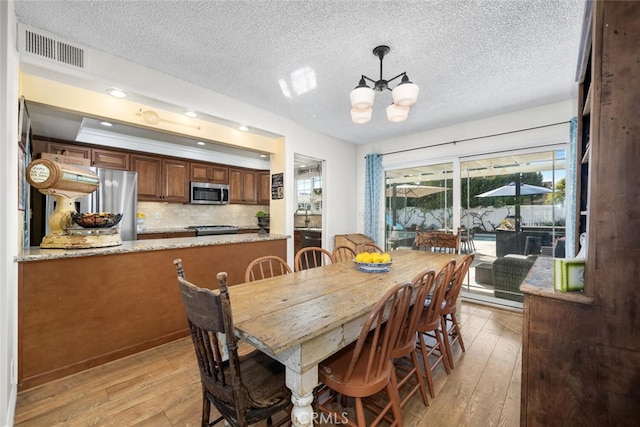 dining space featuring light wood-style flooring, visible vents, a chandelier, and a textured ceiling