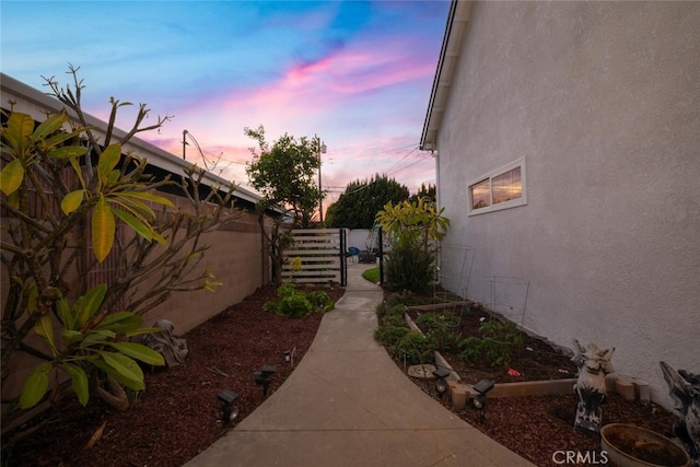 view of side of home featuring fence, a garden, and stucco siding